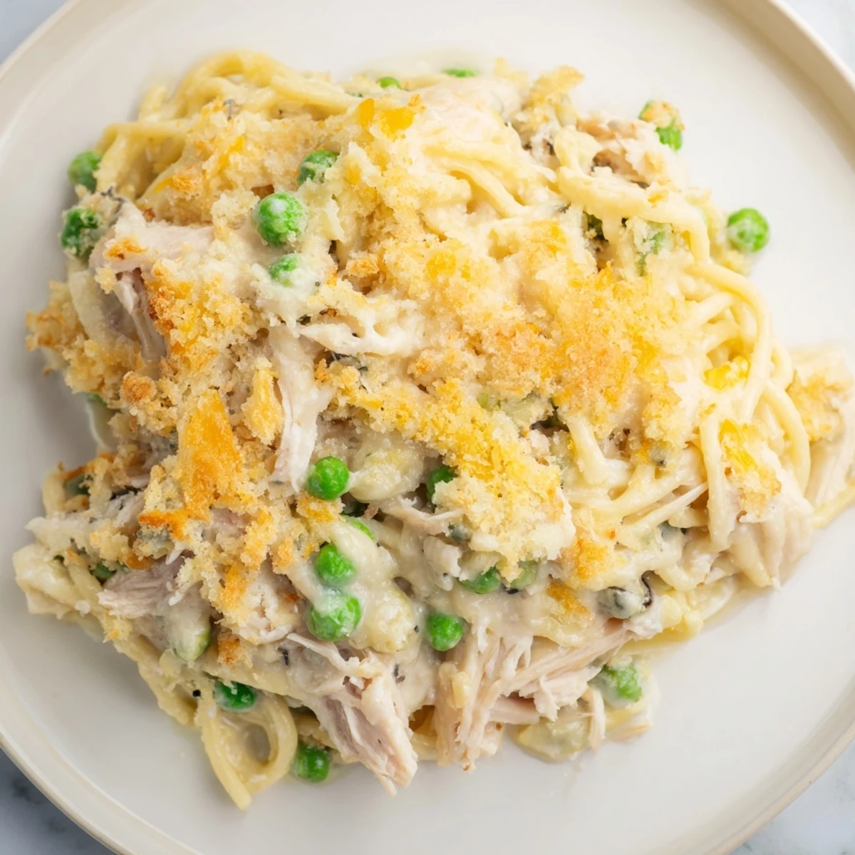 A bubbling Turkey Tetrazzini Bake with a flavorful parmesan crust, featuring visible chunks of chicken and peas.