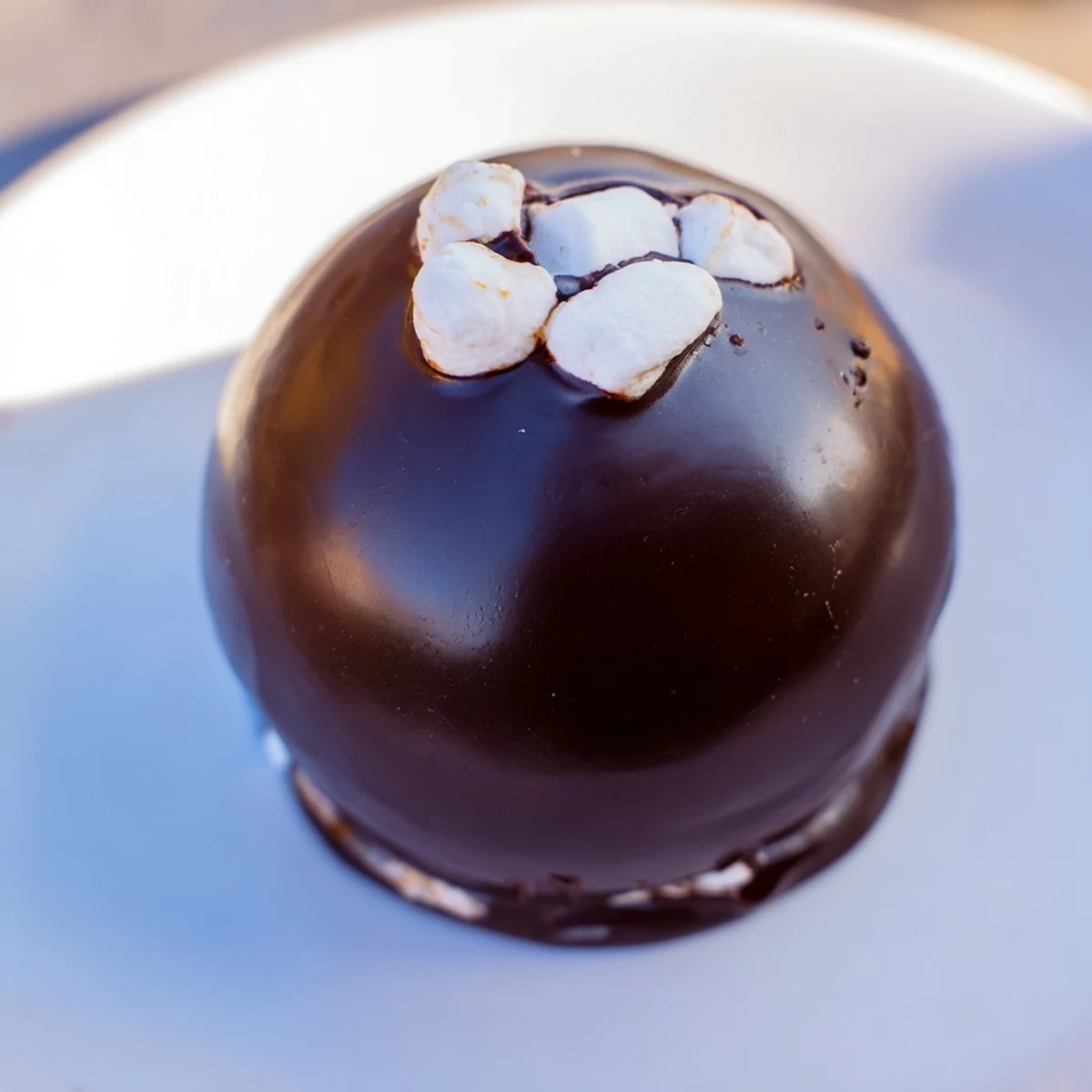 A hand holds a mug where a Hot Chocolate Bomb dissolves in steaming milk, creating a creamy swirl of rich cocoa and marshmallows.
