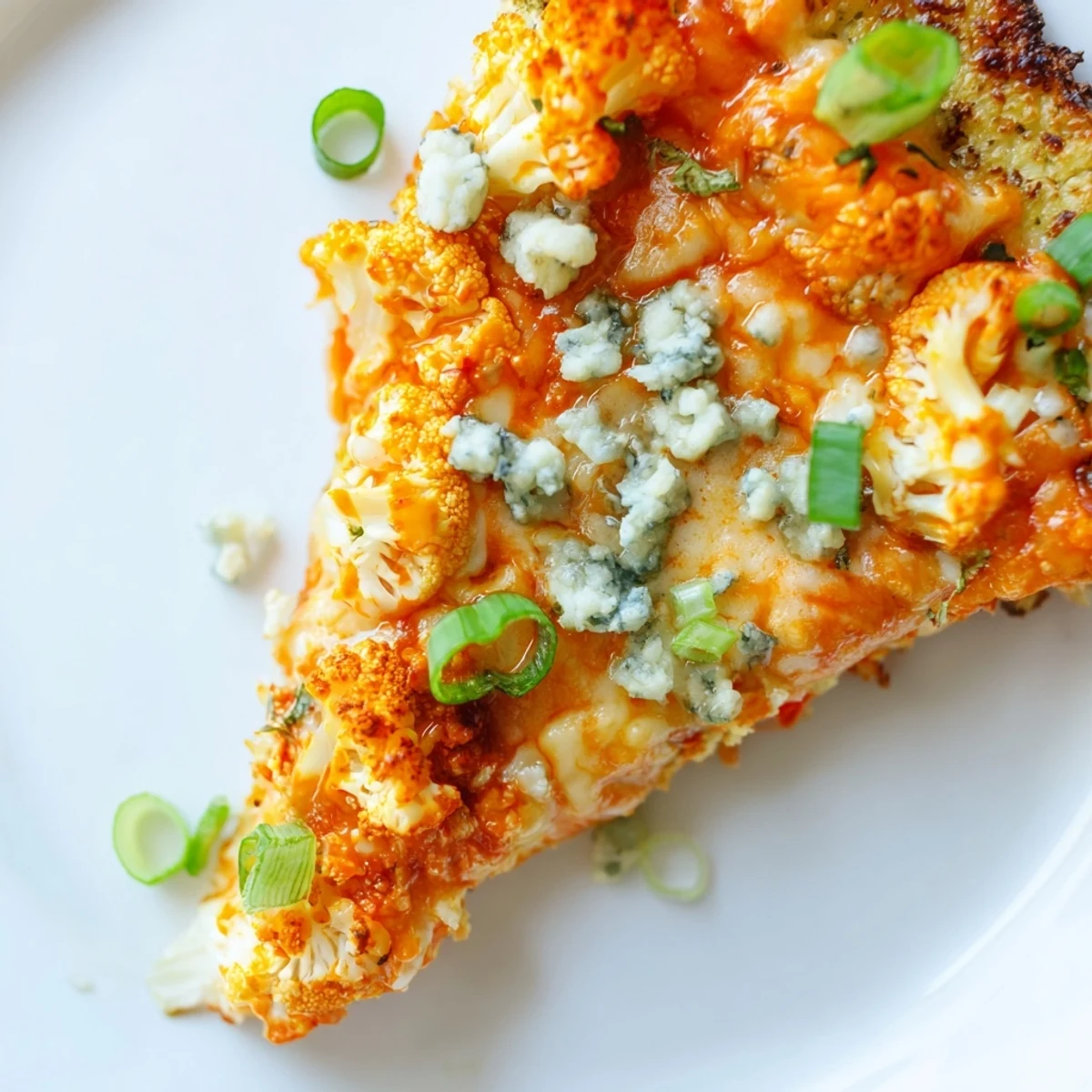 A close-up of a freshly baked Buffalo Cauliflower Pizza slice, showcasing crispy cauliflower crust, melted mozzarella, and vibrant green onions on top.  