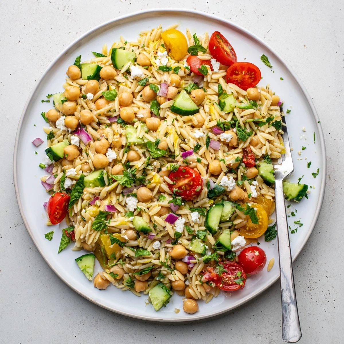 Fresh and vibrant Lemony Chickpea Orzo Salad in a white bowl, featuring chickpeas, cucumber, and cherry tomatoes tossed in a zesty lemon vinaigrette.