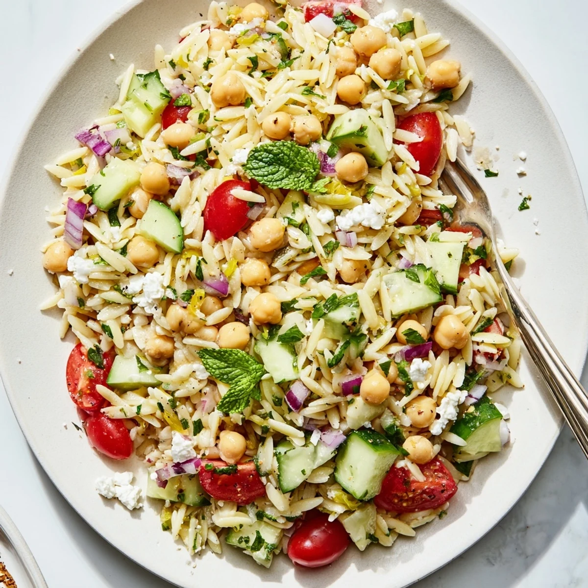 Bright bowl of Lemony Chickpea Orzo Salad with orzo pasta, chickpeas, tomatoes, and cucumber tossed in a golden lemon dressing, ready to eat.