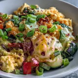 Steam rises from a warm Scrambled Egg and Veggie Bowl topped with melted cheddar.