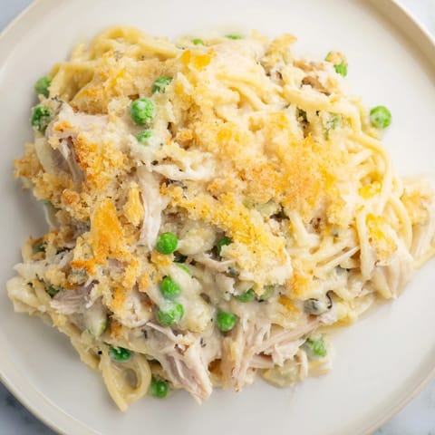 A bubbling Turkey Tetrazzini Bake with a flavorful parmesan crust, featuring visible chunks of chicken and peas.