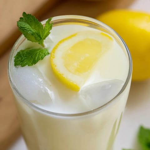 A tall glass of creamy lemonade, layered with frosty ice cubes, lemon slices, and fresh mint leaves on a rustic table.  