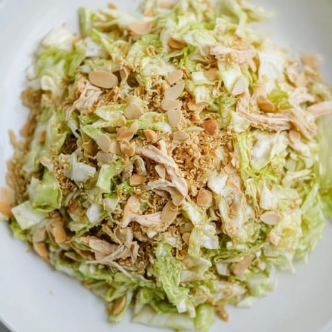A close-up of vibrant ramen chicken salad with carrots and scallions, served fresh in a white bowl.