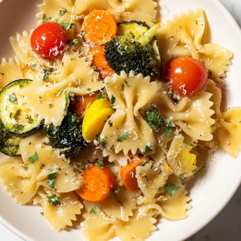 A close-up of rainbow veggie pasta primavera with colorful cherry tomatoes, broccoli, and bow-tie pasta glistening in garlic olive oil.  