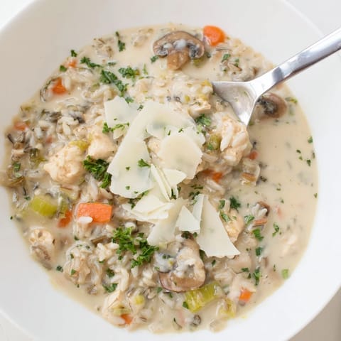 A hearty bowl of Parmesan Mushroom Chicken and Wild Rice Soup is served hot alongside crusty bread for dipping.