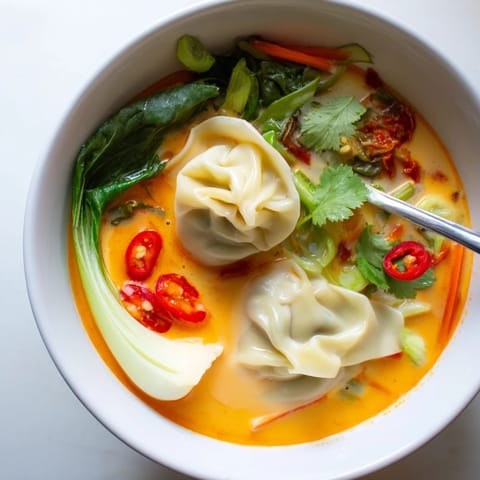 Vibrant Red Curry Wonton Soup served hot, garnished with fresh cilantro and scallions, alongside lime wedges for a zesty, comforting meal.  