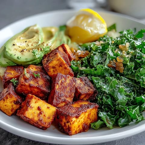 A vibrant Tofu Breakfast Bowl with spiced tofu, bright green kale, and sliced avocado served beside a fresh lemon wedge.