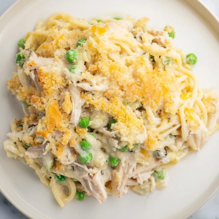 A bubbling Turkey Tetrazzini Bake with a flavorful parmesan crust, featuring visible chunks of chicken and peas.
